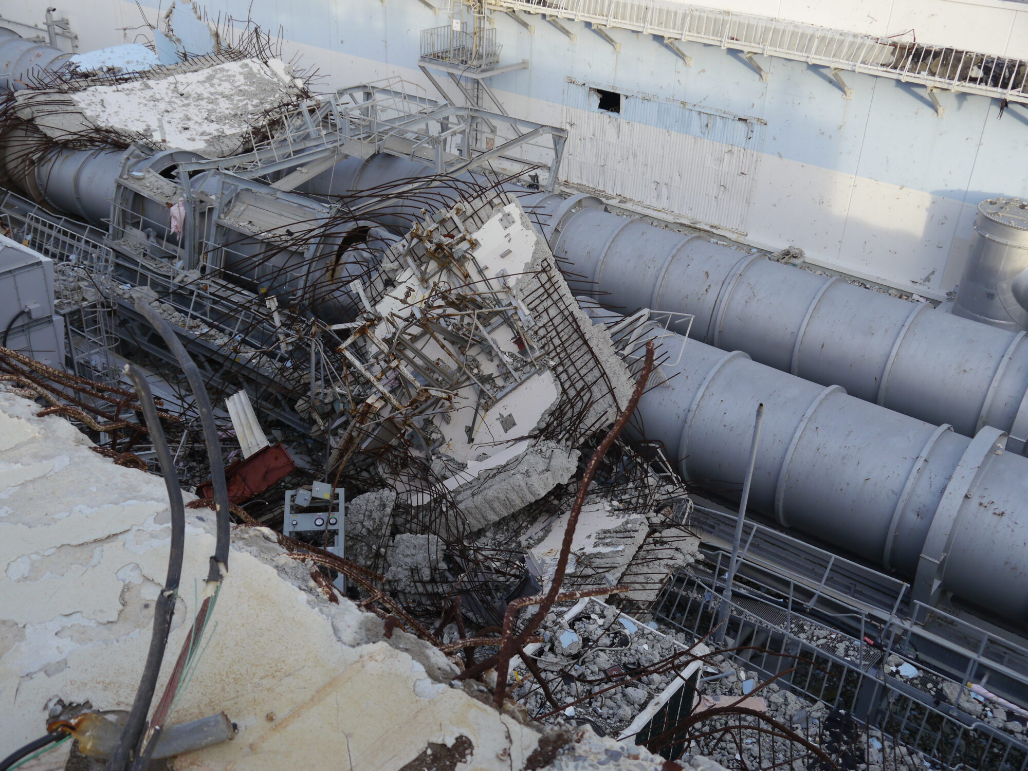 Debris from the upper levels of Unit 4 lies beside the building. The rubble as been cut away to prepare for construction of a new cover, so that fuel can be moved from the unit’s spent fuel pool to a common pool. Fukushima Daiichi Nuclear Power Plant. 18 December 2012